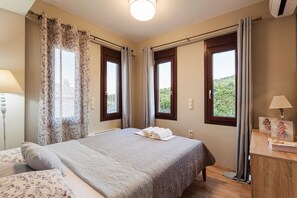 Un dormitorio con cama, dos ventanas, una mesita de noche y una lámpara.