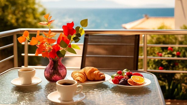 Una mesa con un florero, croissants y fruta en un balcón con vistas panorámicas.