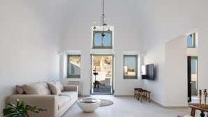 Ein geräumiges Wohnzimmer mit hohen Decken, einem Sofa, einem Couchtisch und einem an der Wand montierten Fernseher.