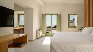Ein modernes Hotelzimmer mit einem großen Bett, einem an der Wand befestigten Fernseher, einem Schreibtisch mit Stuhl und Blick ins Freie durch eine geöffnete Tür.