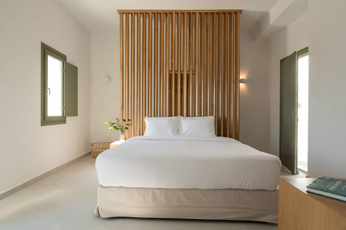 Un dormitorio moderno con una cama grande, un separador de listones de madera, una mesita de noche y una planta pequeña.