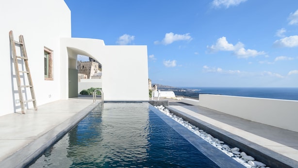 Ein moderner Poolbereich mit freiem Blick auf das Meer, ein weißes Gebäude und eine Holzleiter.