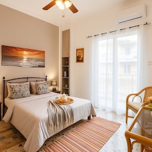 Ein Schlafzimmer mit Bett, Nachttisch, Lampe, Bücherregal und Blick durch ein Fenster nach draußen.