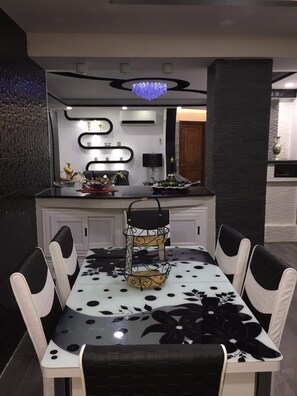 A dining area with a black and white patterned table, white cushioned chairs, a decorative centerpiece, and a modern kitchen in the background.