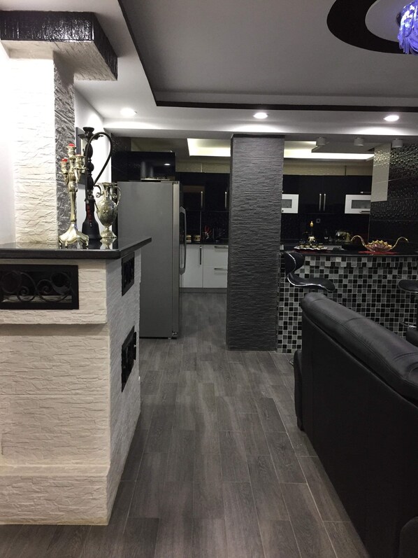 A modern kitchen with a central island, a refrigerator, and a seating area with a black sofa.