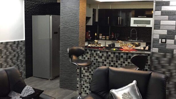 A modern living room with two black leather sofas, a glass coffee table, and a kitchen area with a black and white tiled backsplash. - Rental apartment close to all services. (Bouzareah)