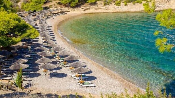 A beach with rows of umbrellas and sun loungers, clear turquoise water, and sparse vegetation. - Thalassa, Return To Timeless Spetses (Spetes)