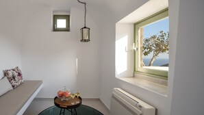 A small, bright room with a window, a radiator, a table with fruit and glasses, and a bench with floral cushions.