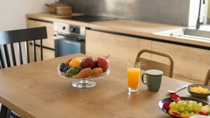A breakfast table with a fruit bowl, a glass of orange juice, a plate of grapes, and a bowl of cereal.