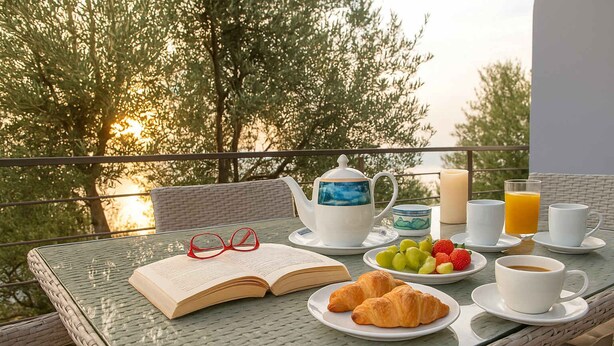 A table set for breakfast with a book, glasses, croissants, fruit, and beverages. - Nina's Villa, Cosy Seaview Retreat (Paralia Vergas)