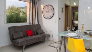 A modern living room with a grey sofa, a glass dining table, and a large wall clock. - Nina's Villa, Cosy Seaview Retreat (Paralia Vergas)