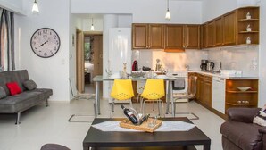A modern living room with a sofa, a dining table with yellow chairs, and a kitchen area with wooden cabinets and a refrigerator. - Nina's Villa, Cosy Seaview Retreat (Paralia Vergas)