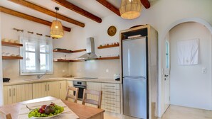 A kitchen with wooden beams, a stainless steel refrigerator, a dining table with a fruit bowl, and a hanging light fixture. - Charming little villa Elena with private pool and sea views! (Paros)