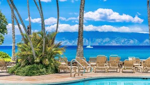 A pool area with lounge chairs and a view of the ocean.