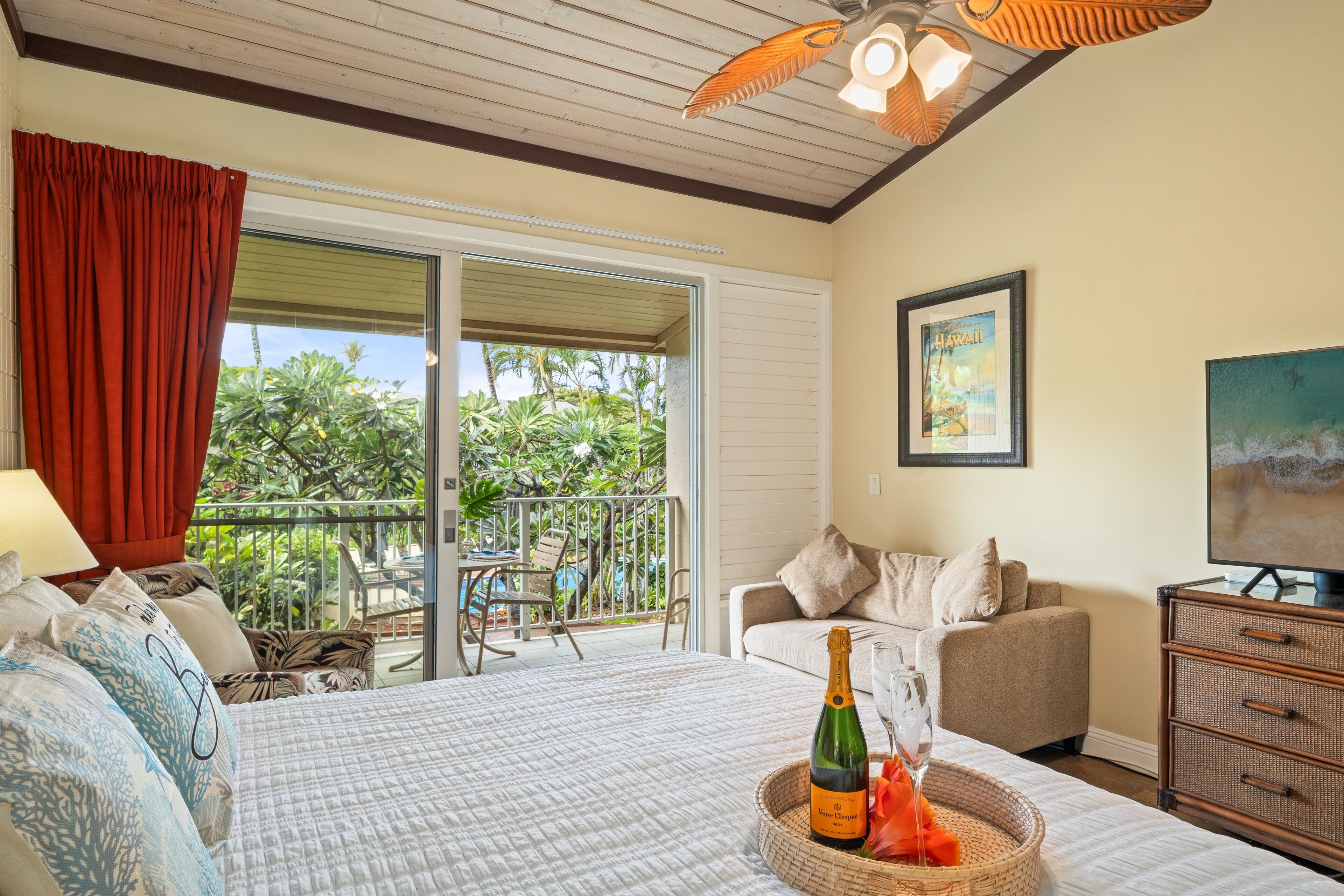 A bedroom with a bed, a nightstand, a television, and a balcony with outdoor furniture.