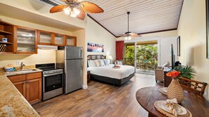 A spacious kitchen with wooden cabinets, a refrigerator, and a stove. There is a dining area with a table and chairs, and a large bed with a view of the outdoors.