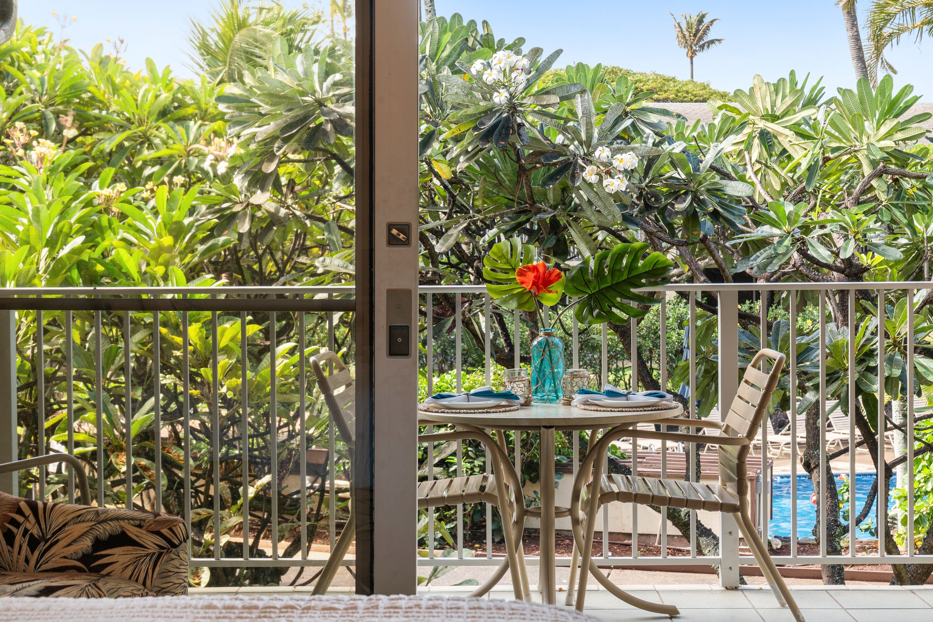 Ein Balkon mit Esstisch, umgeben von üppiger tropischer Vegetation und Blick auf einen Pool.
