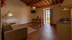 Una sala de estar acogedora con sofá, una mesa de comedor con sillas, una zona de cocina con estufa y un techo con vigas de madera a la vista.