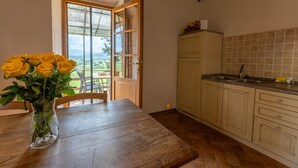 Una cocina con armarios de madera, una mesa de comedor con un jarrón de flores amarillas y vistas a través de una puerta abierta.