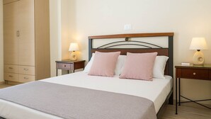A neatly made bed with a wooden headboard, two bedside tables with lamps, and a wardrobe. - Comfy nest in a garden, 1,5km to the sandy beach (Marathopoli)