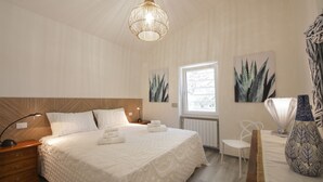 A bedroom with a large bed, a nightstand, a chair, a vase, and wall art. - Villa Cavuzzi (Polignano a Mare)