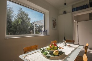 Un comedor con una mesa dispuesta para dos, una ventana con vistas a árboles y un estante montado en la pared con libros.