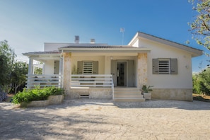 A two-story house with a stone facade, a covered porch with steps, and a small garden area.