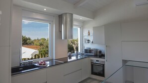A modern kitchen with a large window, stainless steel range hood, and a glass railing overlooking a garden. - Villa Cavuzzi (Polignano a Mare)