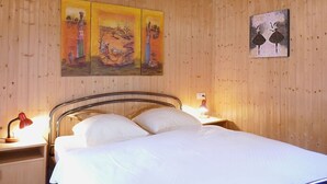 Une pièce aux murs lambrés, comprenant un lit, deux tables de chevet et des œuvres d’art accrochées au mur.