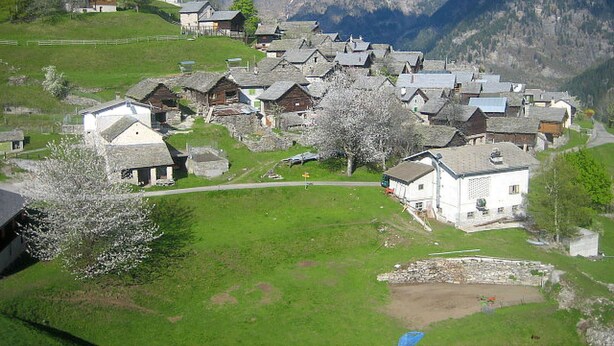 Un village avec des maisons traditionnelles, un petit étang et, en arrière-plan, des montagnes enneigées.