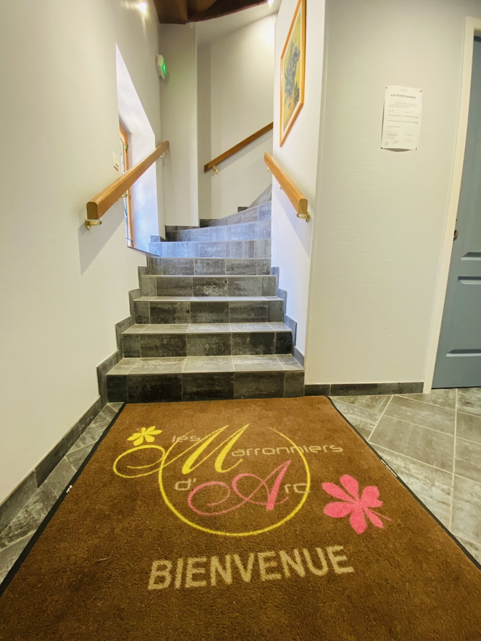 A staircase with a brown welcome mat at the bottom, leading to a room with a blue door and a framed picture on the wall.