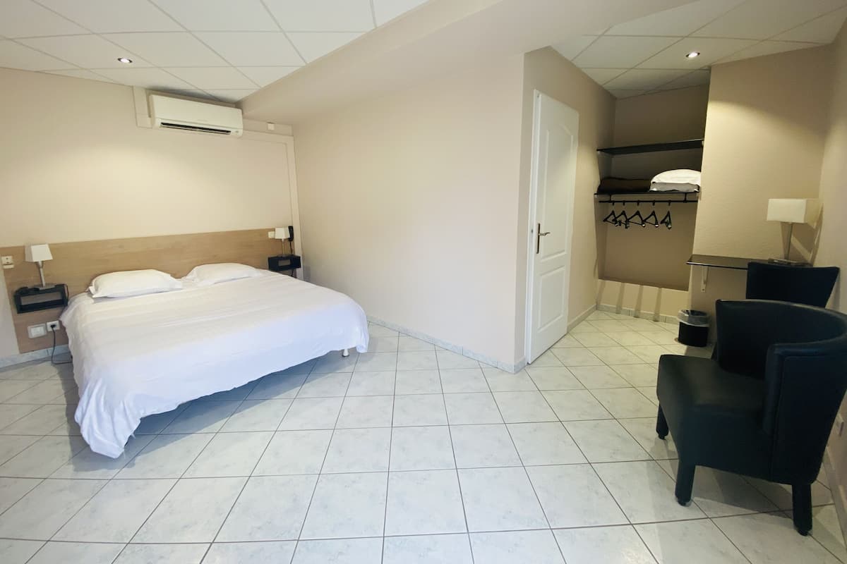 A hotel room with a bed, a chair, a desk, and an air conditioning unit.