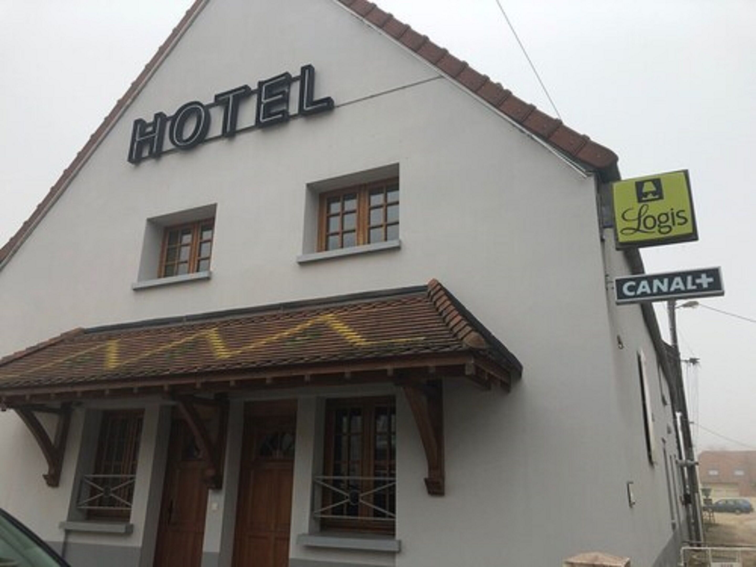 A hotel with a sign reading "HOTEL" above the entrance, a "CANAL+" sign, and a "Logis" sign indicating a business or service nearby.