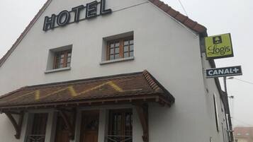 A hotel with a sign reading "HOTEL" above the entrance, a "CANAL+" sign, and a "Logis" sign indicating a business or service nearby.