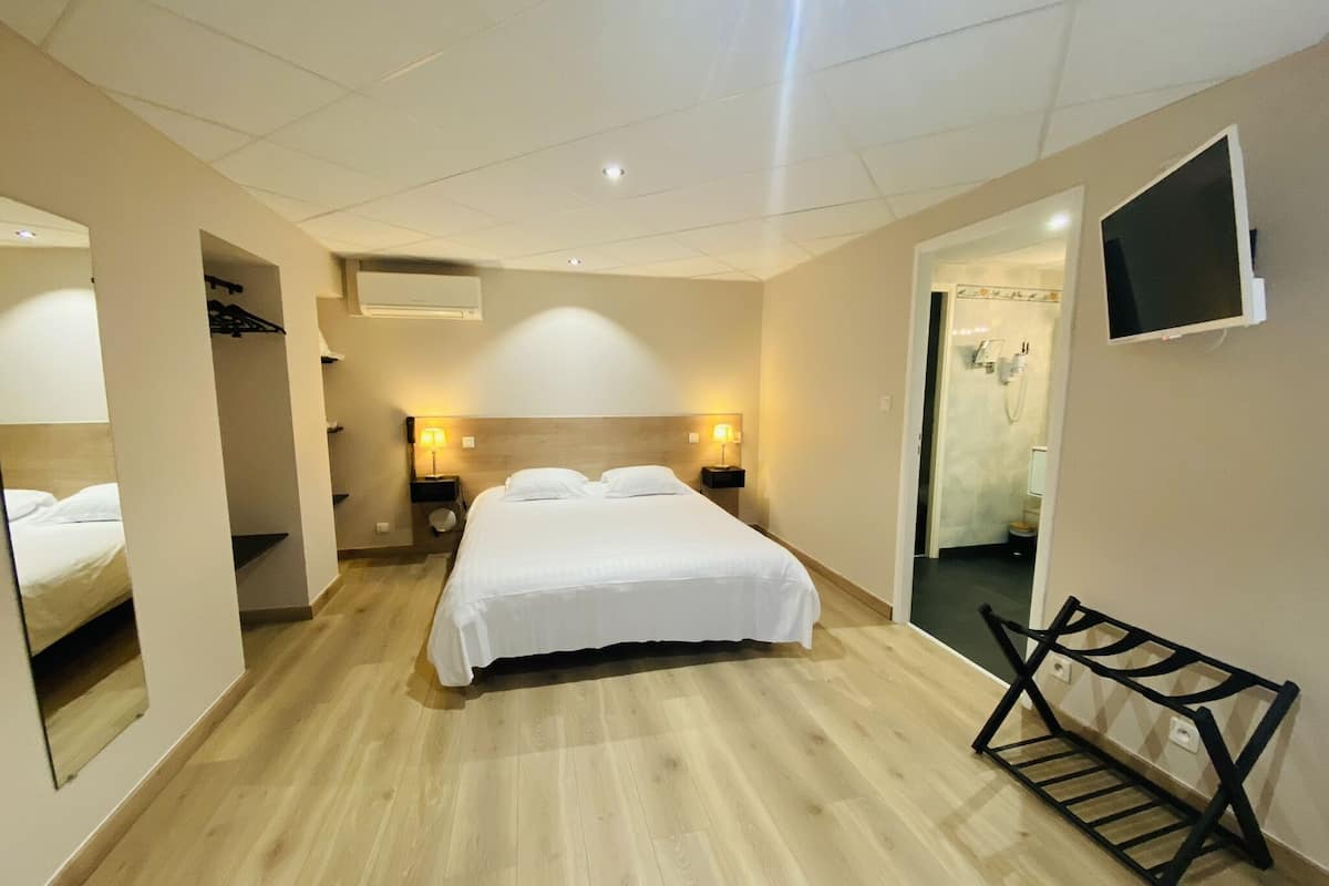 A hotel room with a large bed, bedside lamps, a TV mounted on the wall, and a wooden bench.