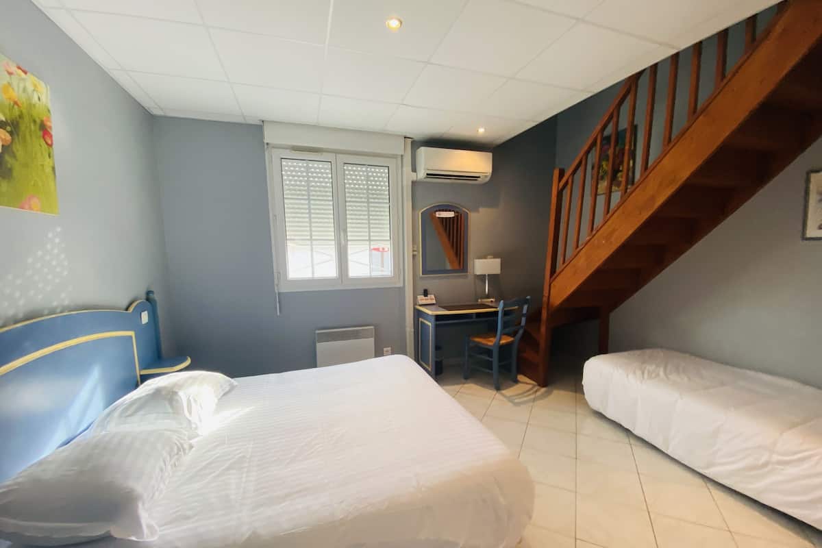 A bedroom with two beds, a desk, a chair, a window, and a staircase.