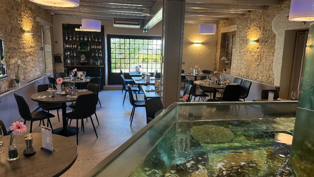 Een restaurant met ronde tafels, stoelen, een bar en een aquarium.