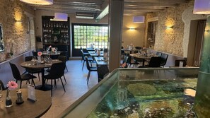 A restaurant with round tables, chairs, a bar area, and a fish tank. - Les Marronniers d'Arc (Arc-sur-Tille)