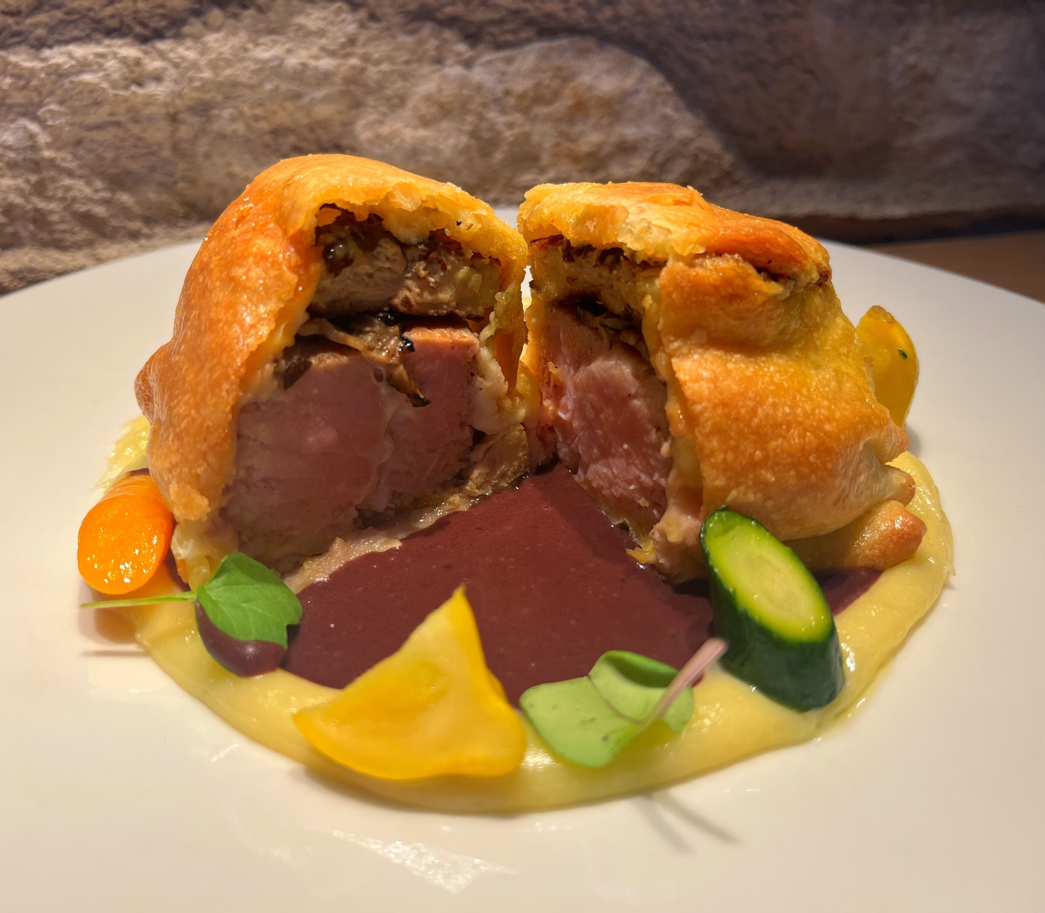 A dish with a golden-brown crust, sliced meat, and garnishes of carrot and cucumber.