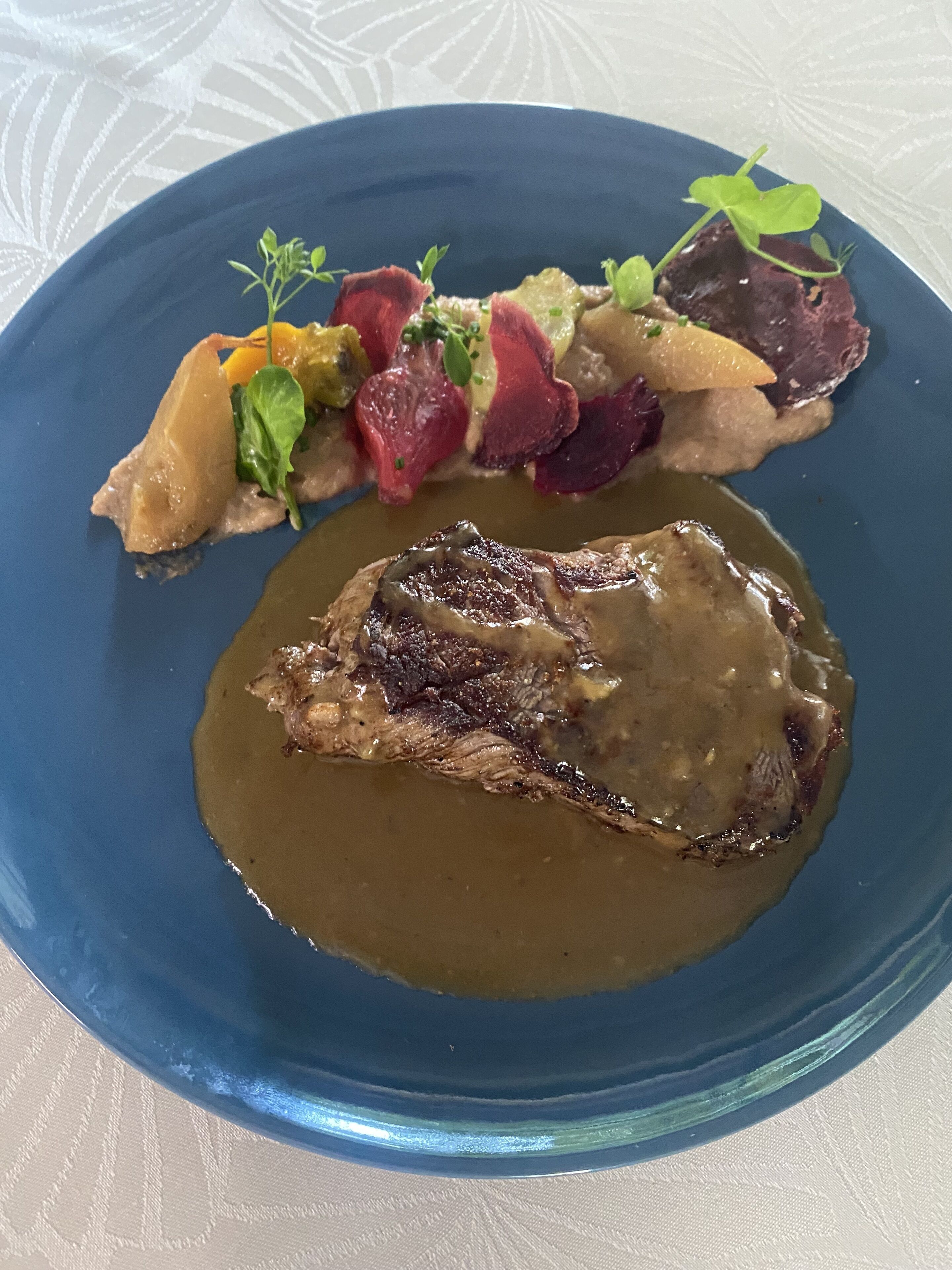 A blue plate with a steak and gravy, accompanied by a side of vegetables and a beetroot slice.