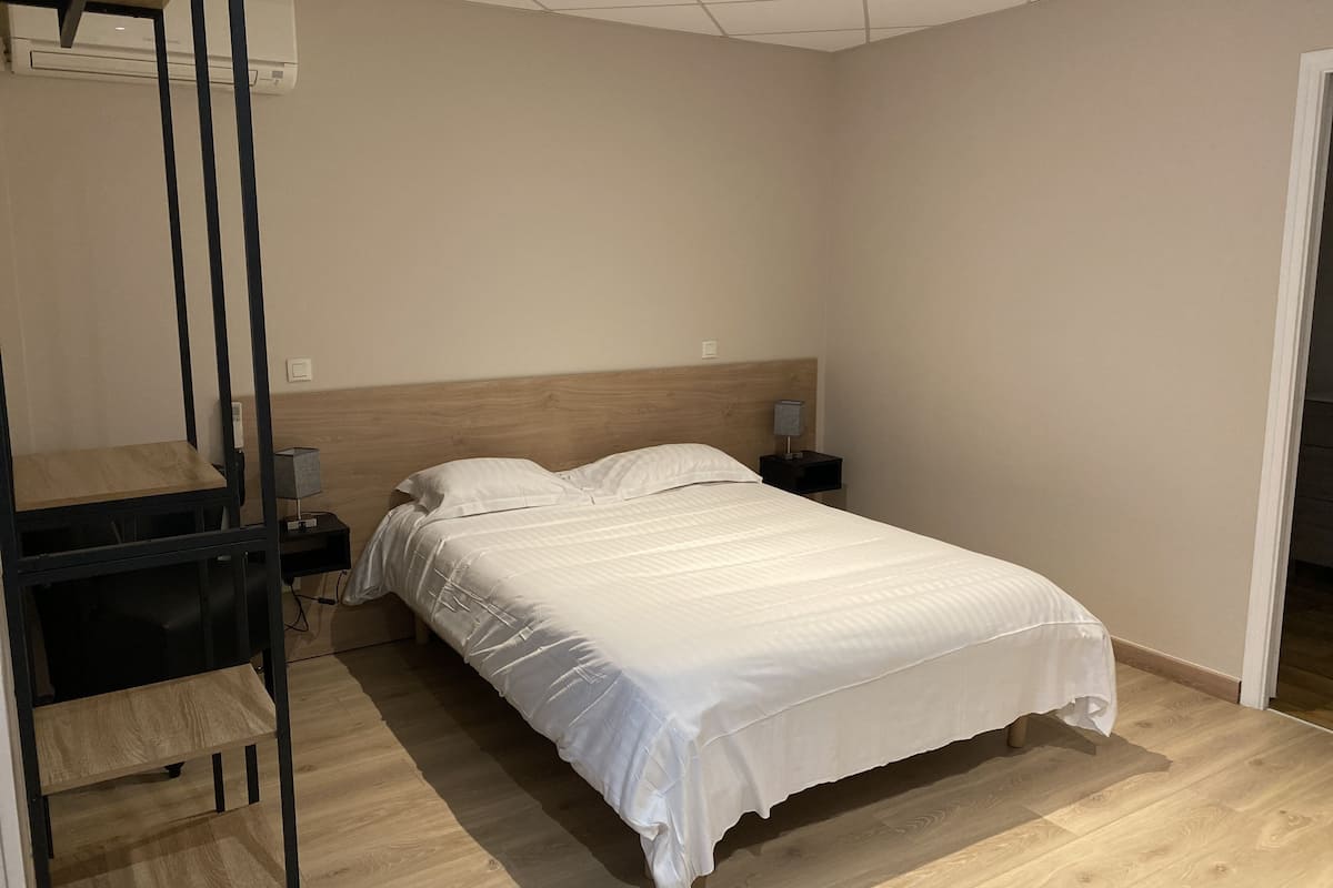 A bedroom with a bed, a nightstand, a lamp, a wooden shelf, and a ceiling fan.
