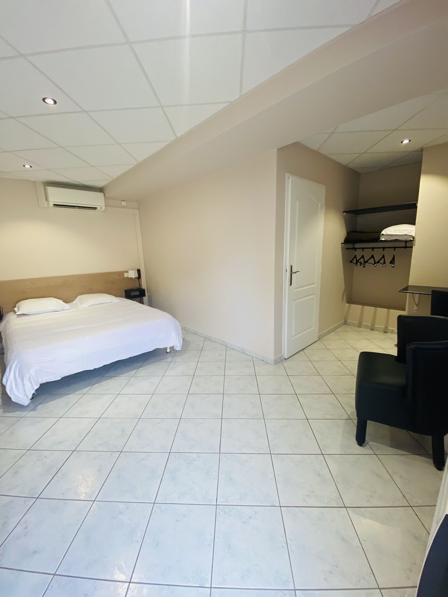 A hotel room with a bed, a chair, a door, and a small seating area with a table.