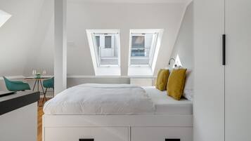 Un dormitorio moderno con tragaluz, una cama con ropa de cama blanca, dos almohadas amarillas y un escritorio con una silla.
