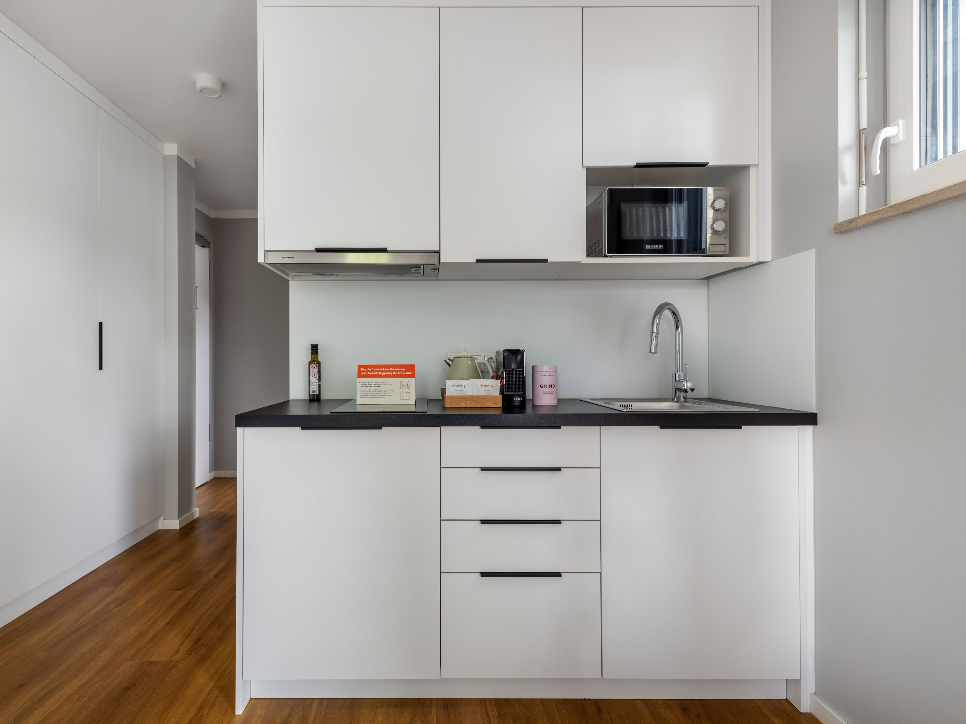 A modern kitchen with white cabinetry, a black countertop, a microwave, a sink, and a coffee maker.