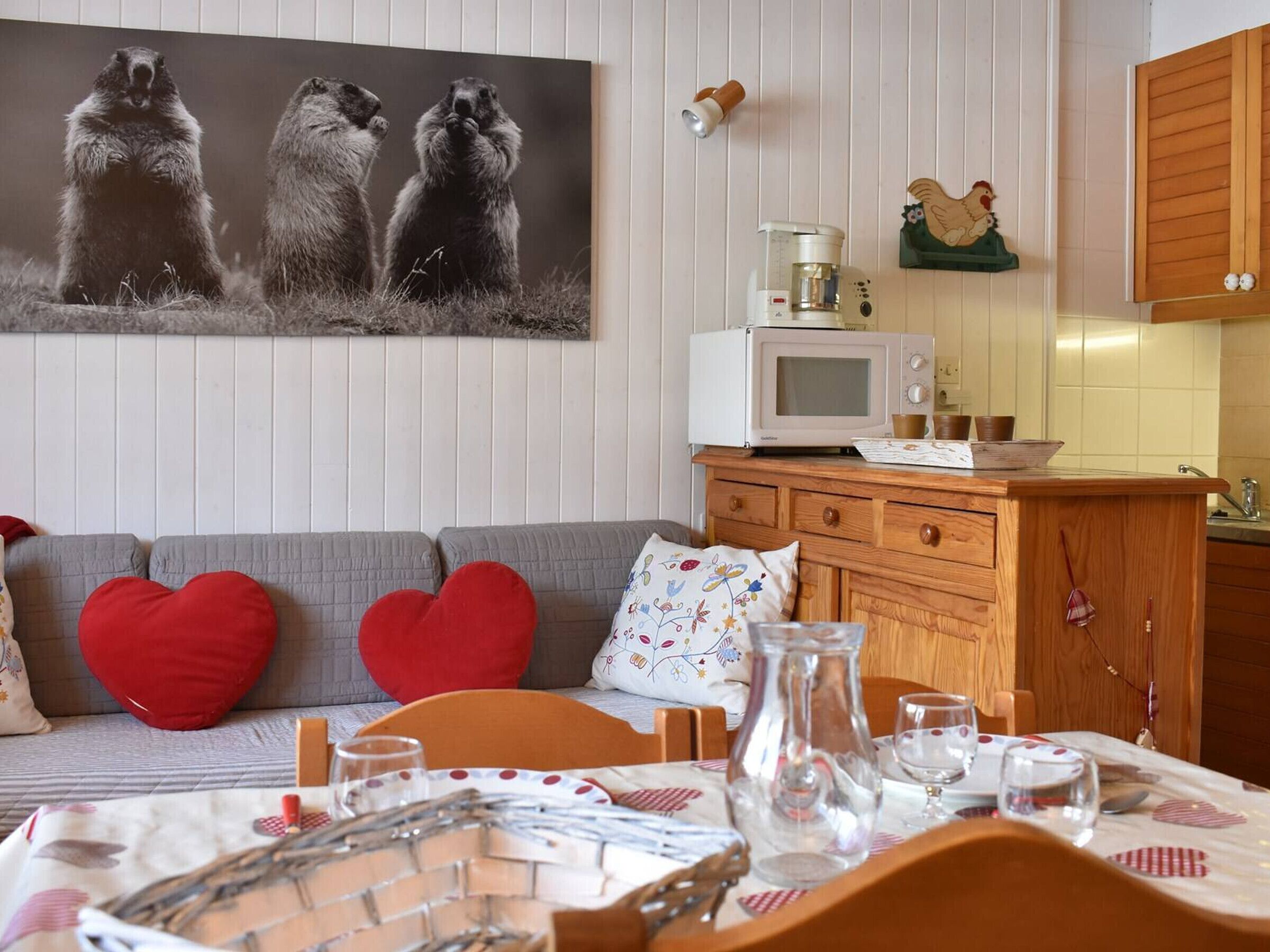 Ett mysigt vardagsrum med en soffa, hjärtformade kuddar, ett soffbord och en matplats med ett bord dukat för två personer.