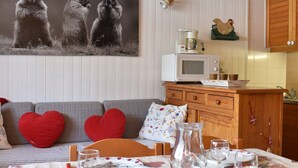 A cozy living room with a sofa, heart-shaped pillows, a coffee table, and a dining area with a table set for two. - Charming Studio for 4 in Meribel, Near Slopes and Shops (Méribel)
