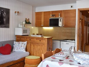 Uma cozinha acolhedora com armários de madeira, micro-ondas, fogão e um espaço de jantar com mesa posta para dois.