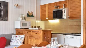 A cozy kitchen with wooden cabinets, a microwave, a stove, and a dining area with a table set for two. - Charming Studio for 4 in Meribel, Near Slopes and Shops (Méribel)