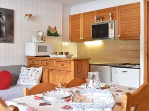 Uma cozinha aconchegante com armários de madeira, micro-ondas, fogão e uma área de jantar com mesa posta para dois.