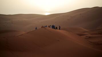 A group of people standing on a sand dune in a desert landscape during sunset.
